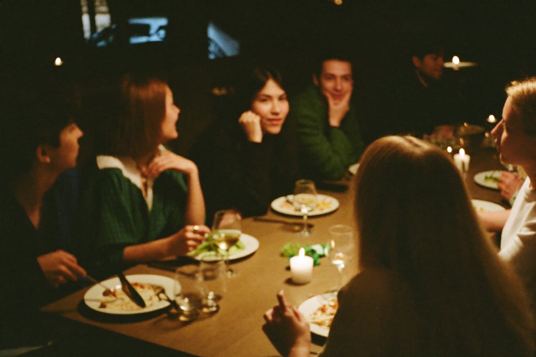 Six people around a restaurant table at night, mid-conversation