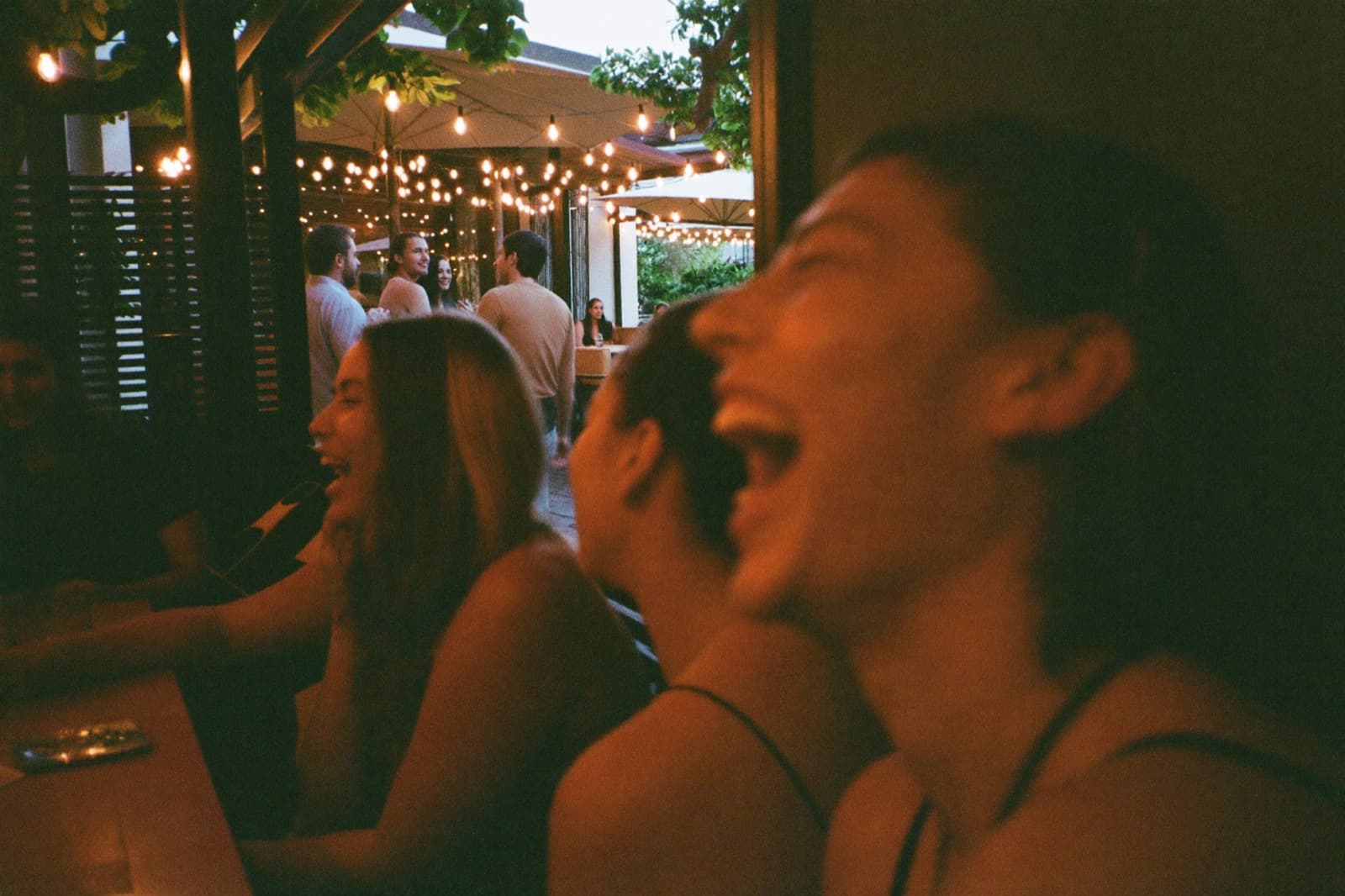 Friends laughing together on a string-lit patio in the evening